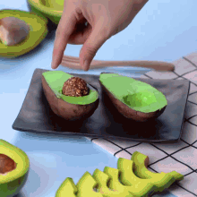 two avocados on a black plate with a hand reaching in