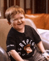 a little boy is sitting in a chair wearing a black shirt that says crypto .
