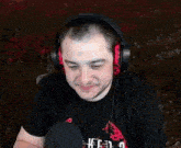 a man wearing headphones and a black shirt is sitting in front of a microphone and smiling .
