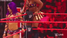 a referee is standing in the middle of a wrestling ring while two women are wrestling .