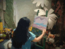 a woman in a blue shirt is holding a painting on an easel