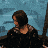 a woman wearing a black jacket with buttons on it looks down