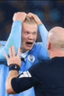 a man in a blue shirt is holding another man 's head while they are playing soccer .