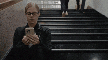 a woman sitting on a set of stairs looking at her cell phone