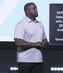 a man in a white under armour shirt stands in front of a large screen