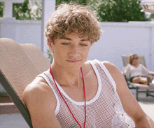 a man wearing a white tank top with a red string around his neck