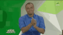 a man in a blue shirt is clapping in front of a green background that says jogo aberto on it