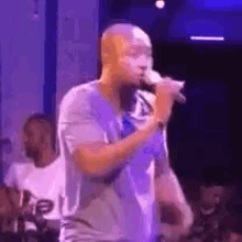 a man is singing into a microphone on stage in front of a crowd .