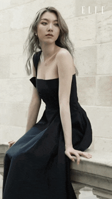 a woman in a black dress is leaning against a wall and the word elle is on the bottom