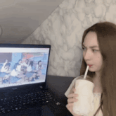a woman drinking through a straw while looking at a laptop