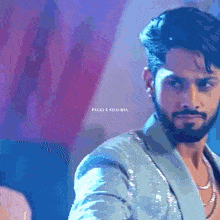 a man with a beard is wearing a blue jacket and a necklace