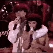 a man and a woman are singing into microphones while standing next to each other .
