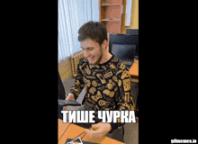 a man wearing a sweater that says ' hello ' on it sits at a desk