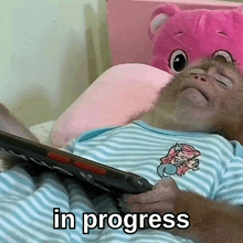 a baby monkey is laying on a bed holding a tablet and the words " in progress " are above it