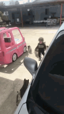 a little boy is standing next to a pink toy car