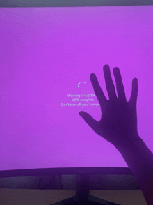 a hand is reaching out towards a purple screen that says working on updates 100 % complete