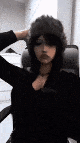 a woman wearing a fur hat is sitting in a chair and taking a selfie .