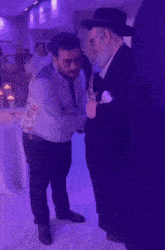 two men are shaking hands in a room with purple lighting