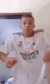 a man wearing a white shirt with the word emirates on it is standing in a room .