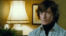 a young man is sitting in front of a lamp and looking at the camera