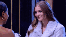 two women are standing next to each other and one is wearing a white fur coat