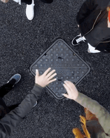 people putting their hands on a manhole cover that says a.c. woodrow & co.