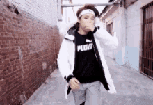 a young man wearing a white jacket and a black t-shirt is standing in a alleyway .