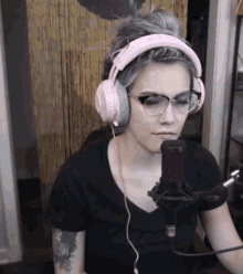 a woman wearing pink headphones and glasses looks at a microphone