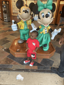 a baby stands in front of a statue of mickey and minnie mouse