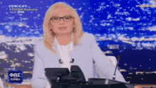 a woman wearing glasses is sitting at a desk with a microphone