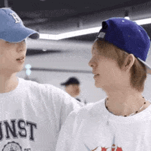 two young men wearing baseball caps are standing next to each other and talking .