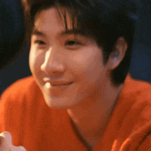 a young man in an orange shirt is smiling and looking at the camera .