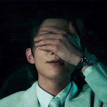 a man in a suit and tie covering his face with his hand