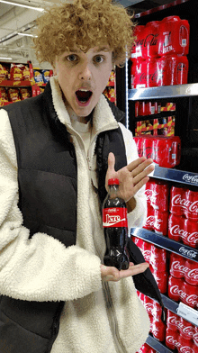 a man is holding a bottle of coca cola in front of a coca cola shelf