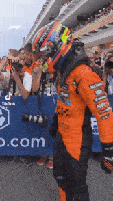 a man wearing a helmet is standing in front of a crowd of people at a race track .