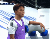 a man wearing a purple adidas vest stands next to a blue pipe