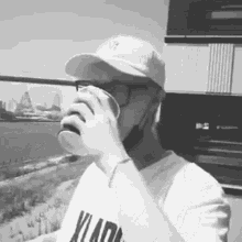 a man wearing a baseball cap and glasses is drinking from a cup .
