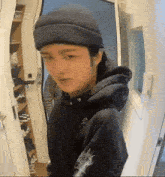 a person wearing a beanie and a hoodie is standing in a hallway .