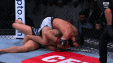two men are wrestling in a cage with a sign that says ufc live in the background