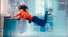 a woman in a red shirt is floating in a kitchen