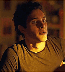 a close up of a man 's face in a dark room wearing a brown t-shirt .