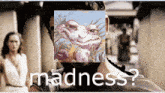 a man with a beard has a picture of a frog in front of his face and the words madness written below him