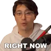 a man wearing glasses stands in front of a microphone with the words right now below him