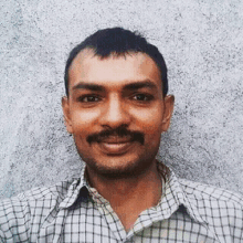 a man with a mustache wearing a plaid shirt smiles for the camera