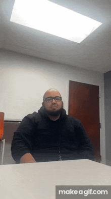 a man with glasses and a beard is sitting at a desk with make a gif.com written below him