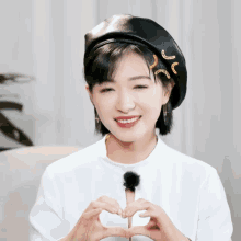 a woman wearing a black beret making a heart with her hands