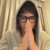 a young man wearing glasses and a hoodie is praying with his hands together