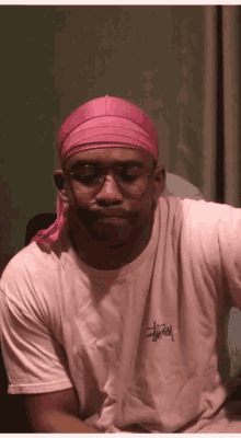 a man wearing a pink headband and glasses is wearing a white shirt with the word stussy on it