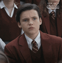 a young man in a suit and tie is sitting in a classroom with the words son of a witch behind him
