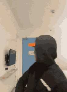 a person wearing a hooded jacket is walking down a hallway with a blue door